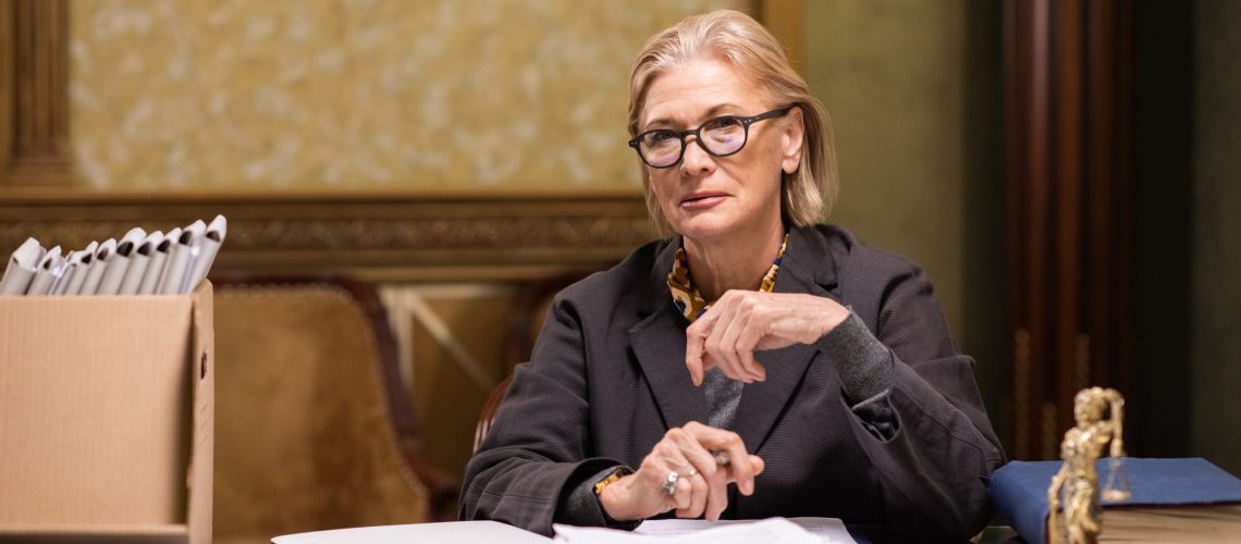 Contemporary lawyer in eyeglasses and formalwear sitting by workplace and looking at camera while working with papers
