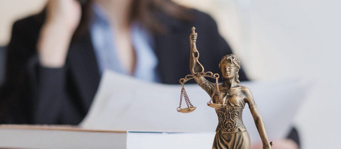 statuette of Themis, goddess of justice. legal advice online, female lawyer in strict suit works in office or court, checks clients' contracts. Caucasian successful business lady.